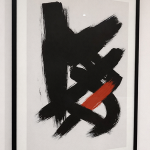 Framed abstract artwork featuring bold black brushstrokes with a single red accent on a white background